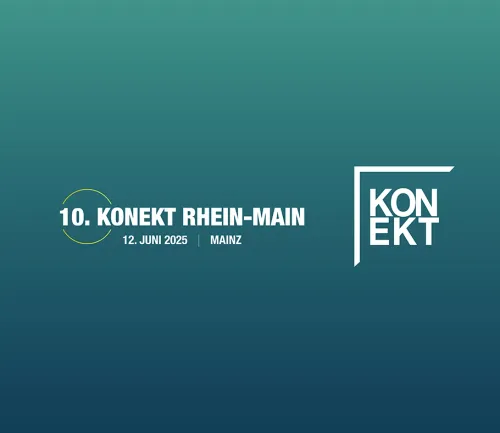 Ein unscharfes Foto mit Gelbfilter. Man sieht das Display eines Handys, mit dem ein Foto einer Personengruppe vor einer Messewand gemacht wird.