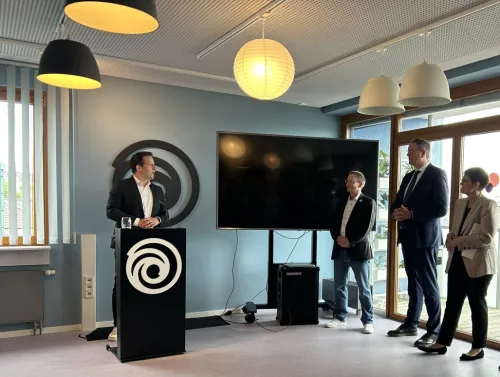 Eine Präsentation, Foto mit Blick auf die Speaker. Deutlich zu sehen unterhalb des Rednerpults ist das Ubisoft-Logo.
