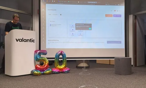 Die Präsentation wird per Beamer an die Leinwand geworfen, in der unteren rechten Ecke sind zwei regenborgenfarbene Ballons platziert, die zusammen die Zahl 50 zeigen.