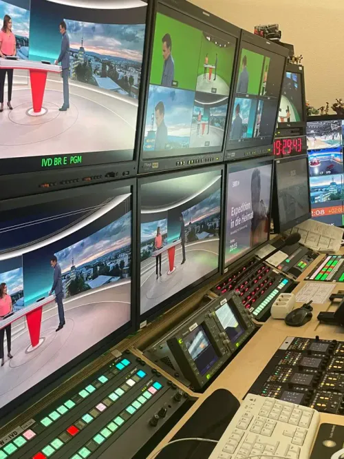 Sechs Bildschirme in zwei Reihen an der Wand, auf denen eine Nachrichtensendung aus verschiedenen Blickwinkeln dargestellt ist; darunter zahllose Knöpfe